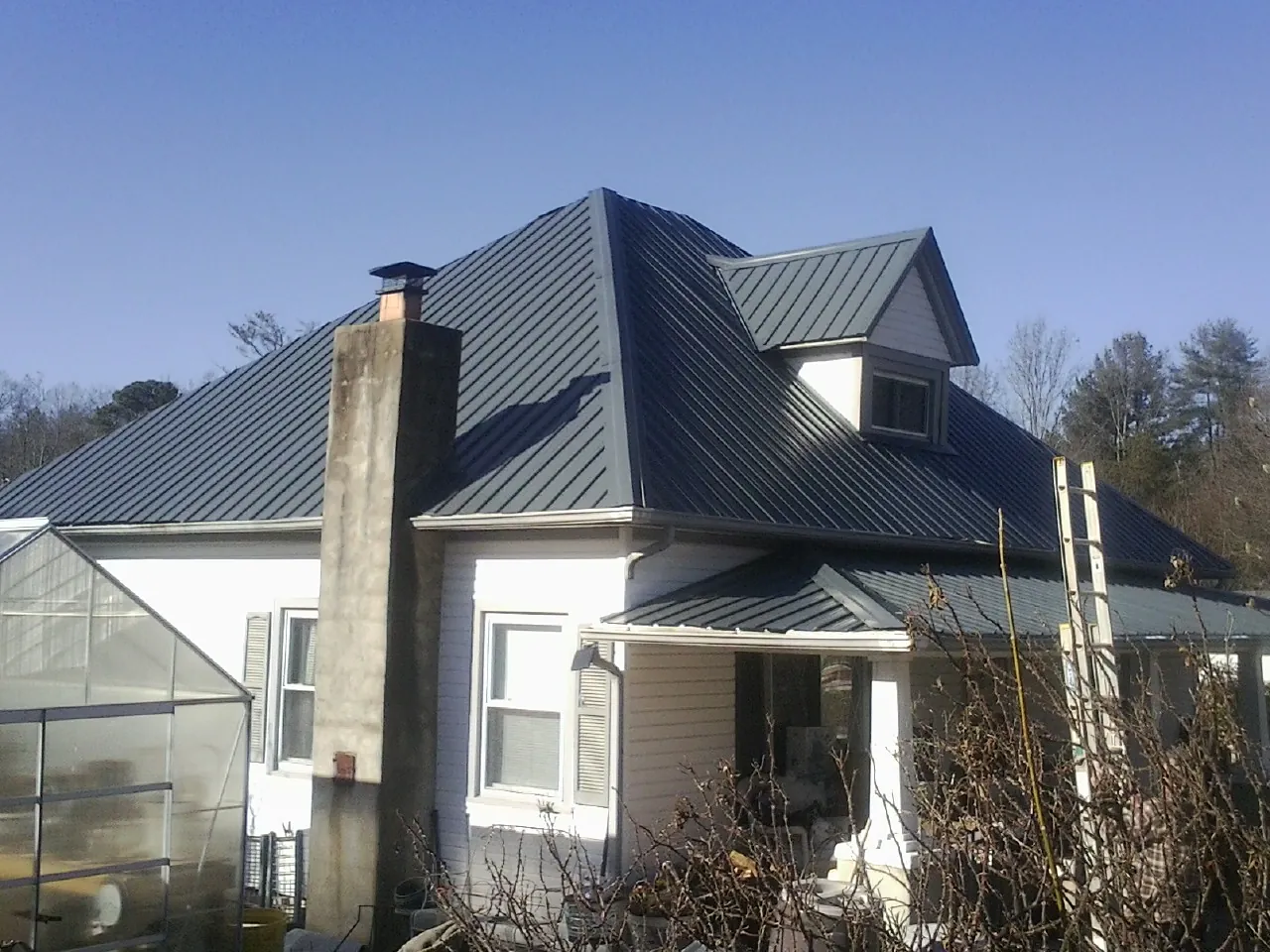 Dark blue standing seam metal roof on a white farmhouse with dormer — Slate & Tile Roof Repair by Roofing Brothers in Hankamer