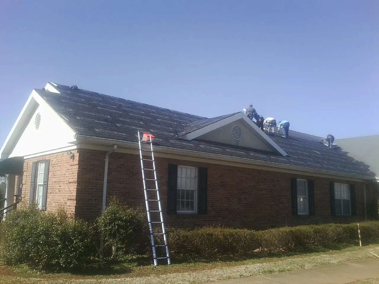 Crew tearing shingles off a brick ranch roof with a ladder set — Metal Roof Repair work by our crew in Hankamer