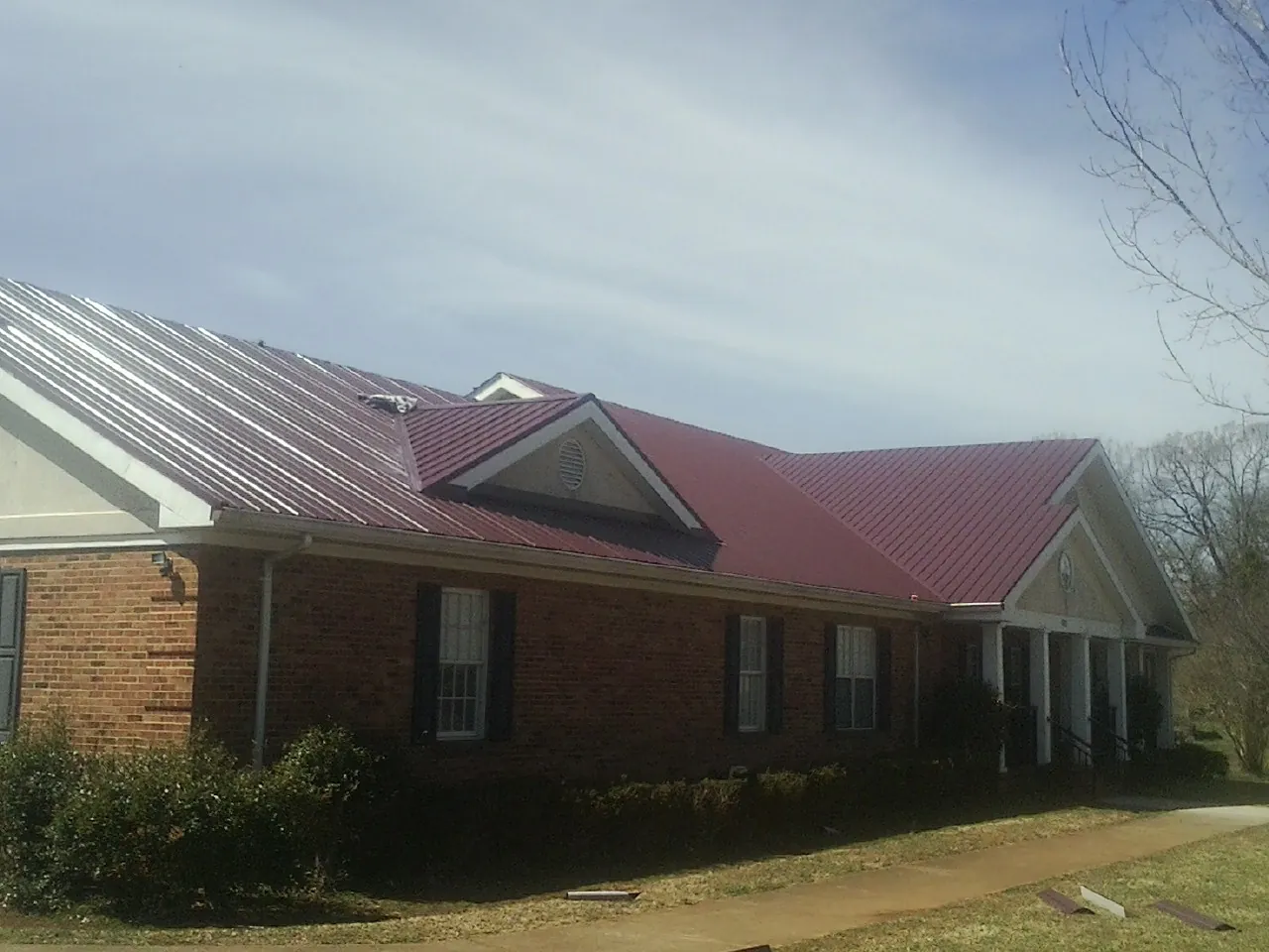 Red metal roof with gabled entries on a long brick building, from a Hail Damage Roof Repair job in Hankamer