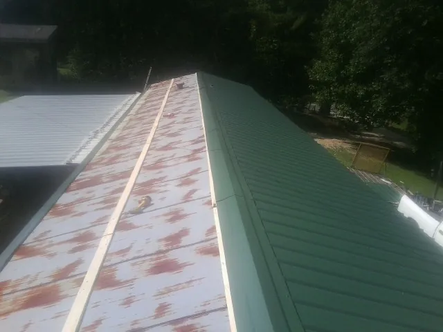 Old rusted panels beside newly installed green metal roofing — Wind Damage Roof Repair by Roofing Brothers in Hankamer
