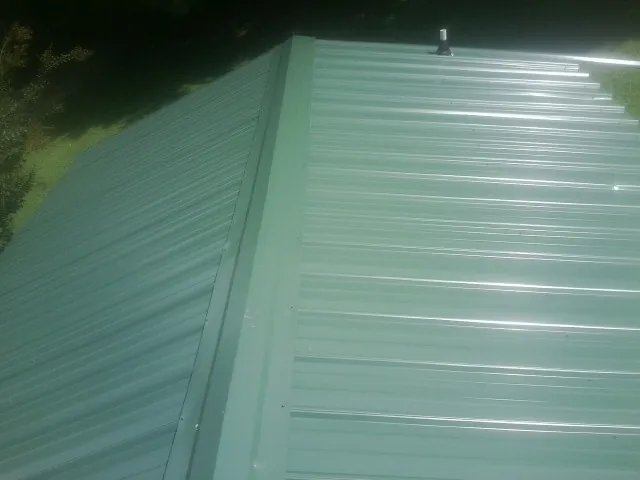 New green metal panels meeting at the ridge of a roof — Flat Roof Repair work by our crew in Hankamer