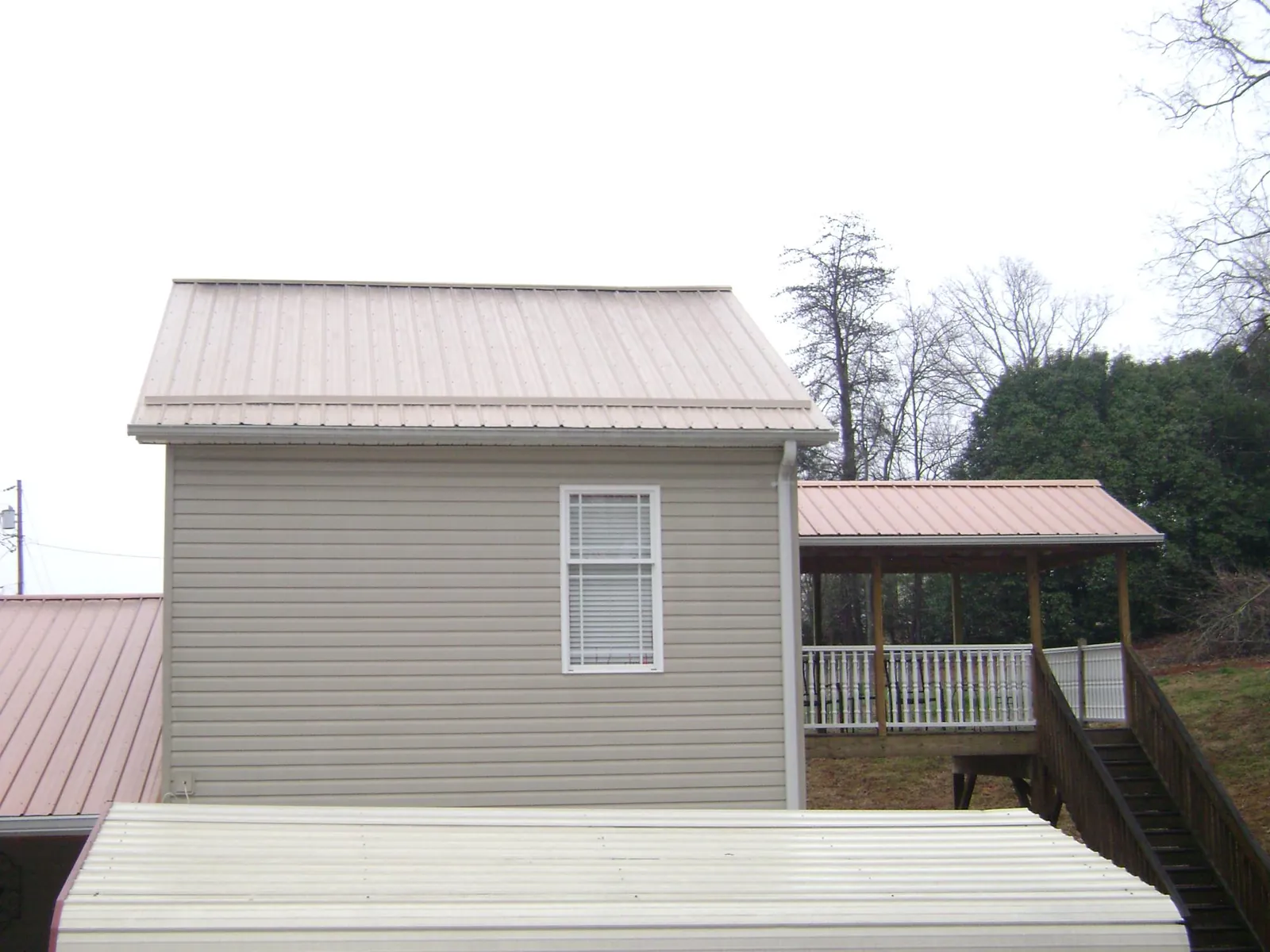 Tan metal roofs on a two story addition and attached porch, from a Roof Replacement job in Hankamer